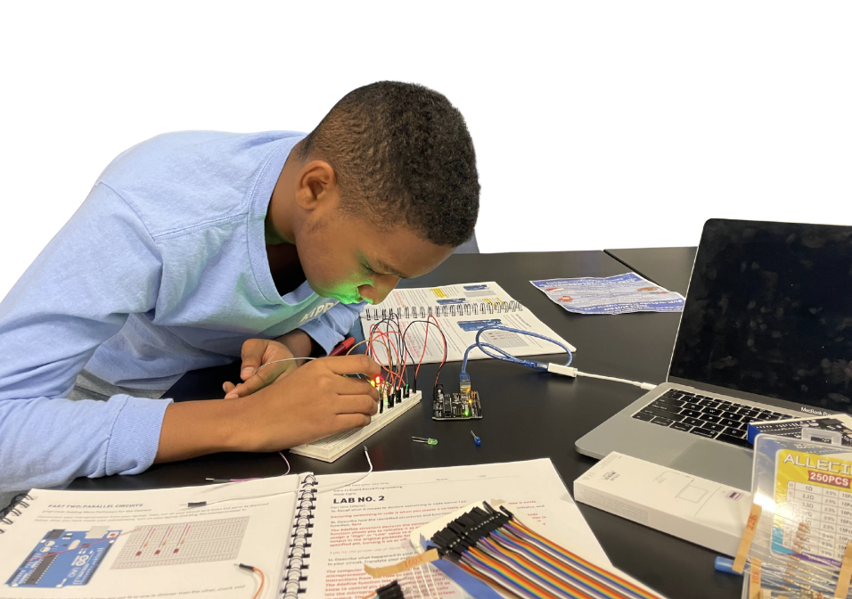 Young students examining circuit boards and electronic sensors on laboratory workbench with laptops displaying data